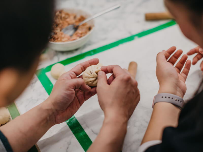 Close up of two people rolling Chinese buns together at a cooking class